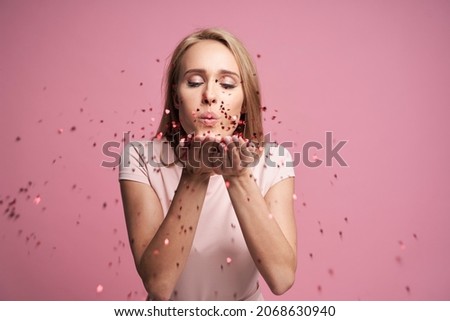 Blonde woman blowing little heart shaped confetti