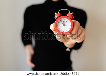 Woman in black shirt holding red alarm clock.