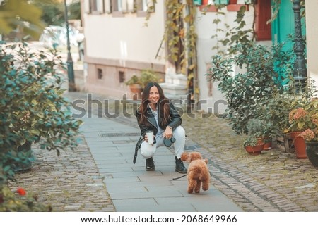 A young beautiful woman with her poodle dog is walking in a European city. Happiness. Little pet. Fall.