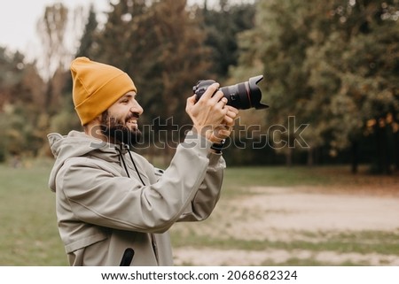 stylish bearded photographer with a camera in his hands takes a photo in the autumn park