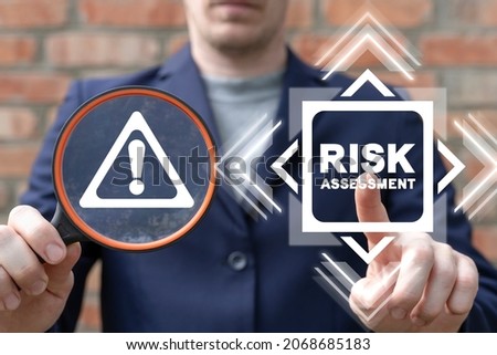 Business concept of risk assessment. Businessman holding magnifying glass with attention sign and using a virtual touchscreen clicks a risk assessment button.