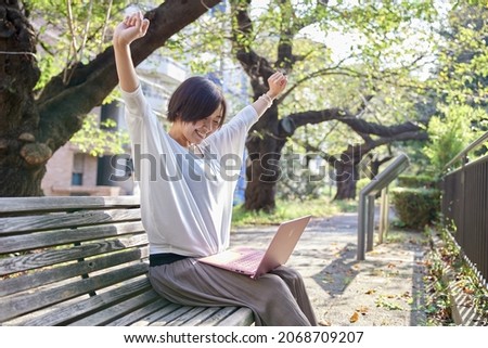 Japanese woman with a laptop sitting on a park bench and stretching