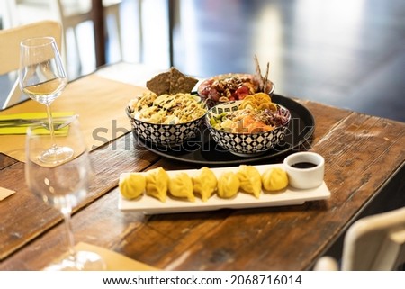 Bowl of poke or marinated seasoned raw fish and steamed ravioli on a set table in a modern fusion restaurant - Oriental fusion food and international cuisine concept Royalty-Free Stock Photo #2068716014