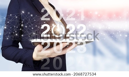 Concept Start New Year 2022. Hand hold white tablet with digital hologram 2022 sign on light blurred background. Happy New Year 2022 - New year 2022, goal, plan, action.
