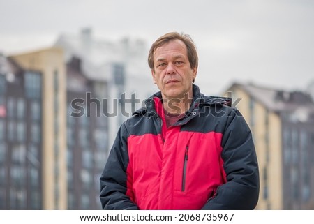 Street portrait of a 45-50-year-old man with a serious expression on the background of urban high-rise buildings, medium plan. Maybe he is a military pensioner or an actor, a truck driver, a buyer. Royalty-Free Stock Photo #2068735967