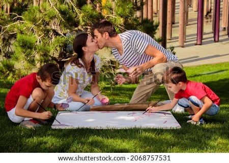 family painting class outdoors in the park on a warm summer day. Mom and Dad kiss, love and happiness