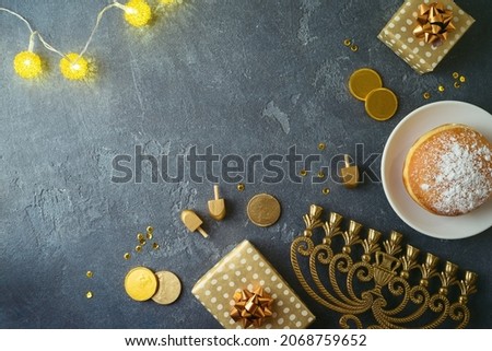 Jewish holiday Hanukkah concept with traditional donuts, menorah and gift box on dark background. Top view with copy space