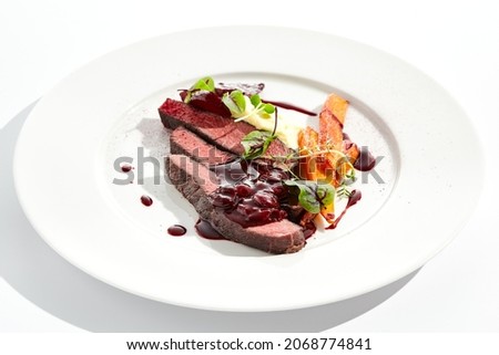 Venison steak with baked vegetables isolated on white plate. Meat steak medium rare roasted with carrot, beetroot and mashed potatoes with cherry sauce. Wild meat in restaurant menu Royalty-Free Stock Photo #2068774841