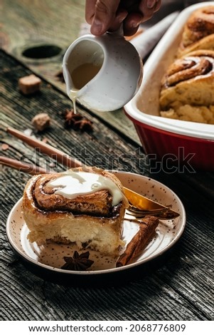 Cinnabon. Woman's hand spreading vanilla icing freshly baked cinnamon rolls, vertical image. top view. place for text.