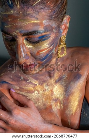 Modelling photography of a young female model with a colourful makeup art presentation over the face. Tribal face colouring woman isolated on the white background.  