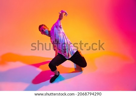 Modern dance art. Sportive boy dancing hip-hop isolated over gradient yellow pink studio background in neon light. Concept of dance, youth, hobby, dynamics, movement, action, ad