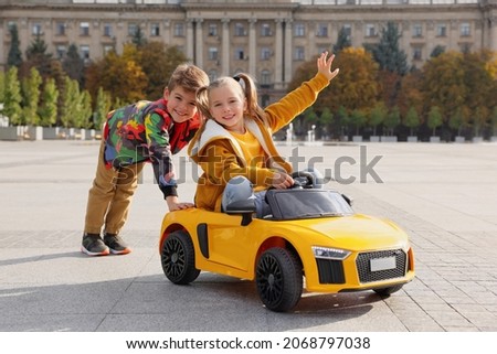 Cute boy pushing children's car with little girl outdoors on sunny day