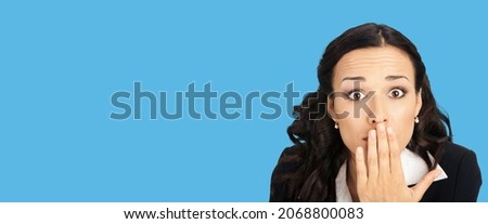 Unbelievable news! Excited surprised, shocked businesswoman in black confident suit. Astonished business woman covering mouth by her hand. Bright blue color background. Wide banner composition.