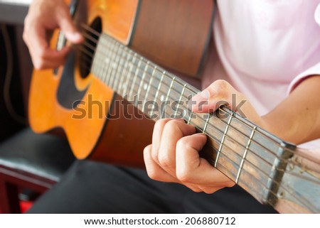 Closeup man's hands playing acoustic guitar with piano background.