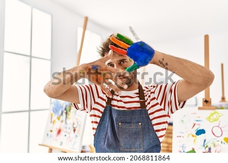 Young hispanic man smiling confident doing picture gesture with hands at art studio