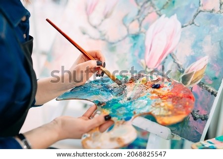 Talented kid holding a professional palette with multi colored paints while working on his new picture in a studio