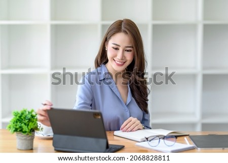 Beautiful young Asian businesswoman smiling using tablet computer working at the office.