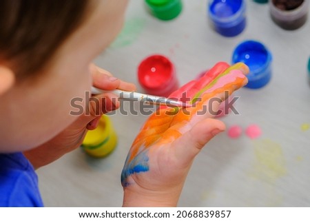 close-up of a child's hand with orange paint. The boy paints his hand with a brush. The idea is children's creativity, self-expression, children's development through drawing. horizontal photo.