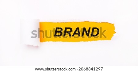 On a bright yellow background, white paper with a torn stripe and the inscription BRAND