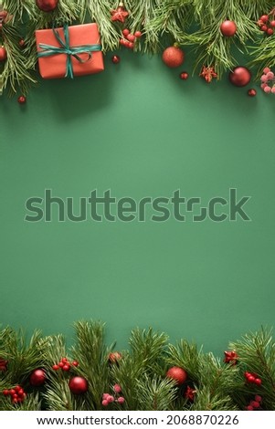 Christmas green background with red gift and evergreen pine branches, red festive baubles. Xmas greeting card. Happy New Year. Space for text. View from above, flat lay.