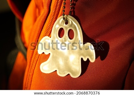 Elegant white reflective safety signal in a ghost pattern form on an orange backpack for pedestrian visibility. Accessory essential for a walker or passerby to walk on the dark street. Royalty-Free Stock Photo #2068870376