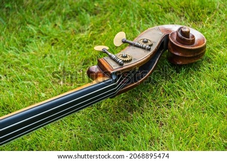 Contrabass on a background of green grass. The musical instrument consists of a soundboard with two holes, a neck with a fretless fingerboard and a headstock in the characteristic shape of a snail. Royalty-Free Stock Photo #2068895474