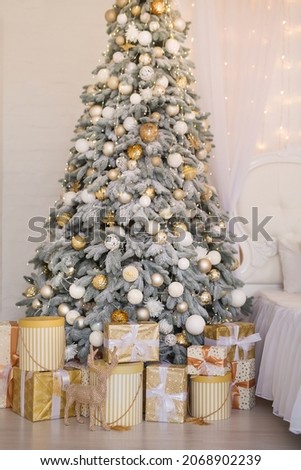 Photo of luxury gift boxes under Christmas tree, New Year home decorations, golden wrapping of Santa presents, festive tree decorated with garland, baubles, traditional celebration