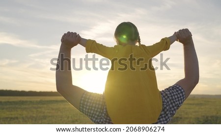 cheerful little kid rides his father at sunset, joyful child sits on his dad shoulders in sunshine of sun, happy family, girl with parent on a weekend trip, childhood dream of being pilot and flying