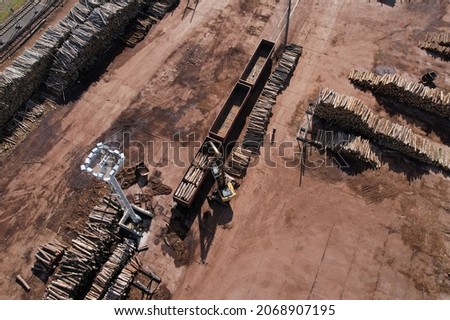 Excavator with log grab crane unloads timber from freight car. Crane with claw loads logs onto log train for lumber mill. Illegal logging and timber export. Wood Machine and Log Grabbing. Royalty-Free Stock Photo #2068907195