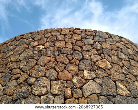 Dry wall built with brown and black blocks of lava (without use of mortar or cement) in background of blue sky in Lanzarote, Canary islands. Old stone masonry textured background. Open joint stonework Royalty-Free Stock Photo #2068927085