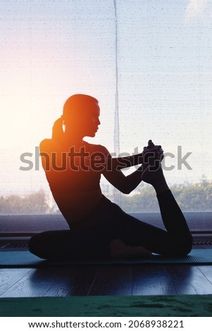 Young woman silhouette doing yoga at home in orange sunset