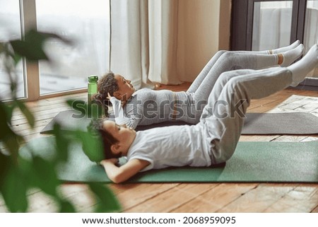 Slim woman and boy are lying on mat and doing abdominal crunches together at home