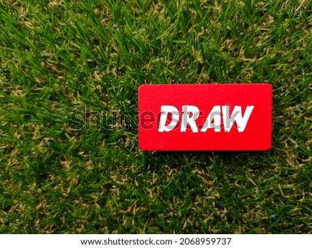 Colored wooden board written with text DRAW on a green grass background. Sport and football concept.
