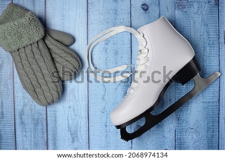 One white figure skate and warm woolen mittens on a blue wooden background. Conceptual photo: Winter, sports, hobbies, healthy lifestyle. Top view, flat lay.