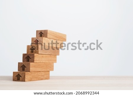 Rise up arrows on wooden blocks arranged as a steps chart on a wooden desk and clean white background with copy space, minimall style. Business growth process and economic improvement concept.
