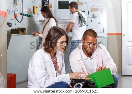 Young friends solving conundrum in quest room in view as closed nuclear bunker, inspecting battery charger Royalty-Free Stock Photo #2069011625