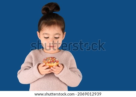 Little happy cute girl eating donuts on isolated blue background.