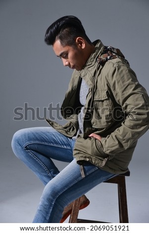 portrait of a male in coat ,jeans sitting chair isolated on gray background