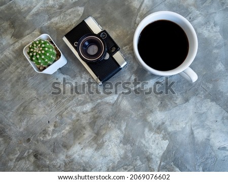 photo above Cactus, white cup hot coffee black Americano without sugar it is popular to drink in morning to help them stay awake  ready to work. and classic camera on table cement pattern Loft color
