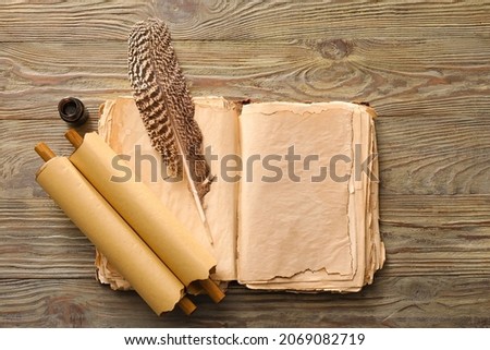 Open old book with scrolls, ink and feather on wooden background