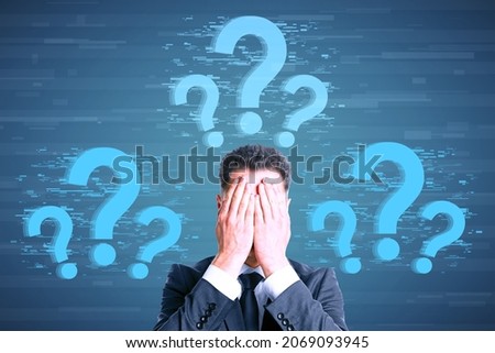 Attractive young caucasian businessman covering eyes with glowing question marks on digital background. FAQ and solution concept