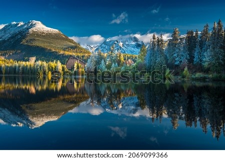 Autumn morning at Strbske pleso with a beautiful calm lake with icicles on colorful trees and snow-capped mountains. Vysoke Tatry, Slovakia, High Tatras