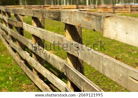 Wooden fence on the farm. A hedge of boards in summer. An obstacle for farm animals.