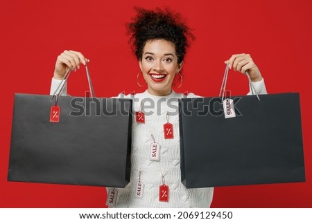 Young costumer woman wear white knitted sweater with tags sale in store showroom hold package bags with purchases after shopping sale written text inscription isolated on plain red background studio