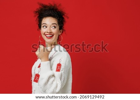 Side view young happy costumer woman wear white knitted sweater with tags sale in store showroom point thub finger aside on workspace area mock up copy space isolated on plain red background studio