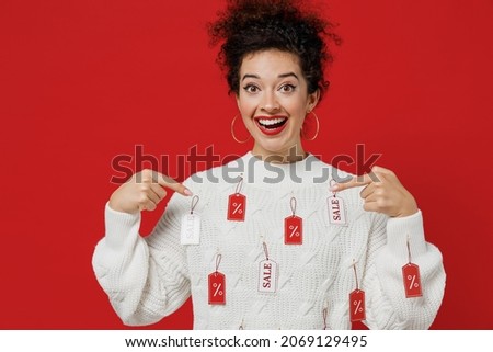 Young smiling surprised fun happy female costumer woman 20s wear white knitted sweater with tags sale in store showroom point index fingre on herself isolated on plain red background studio portrait