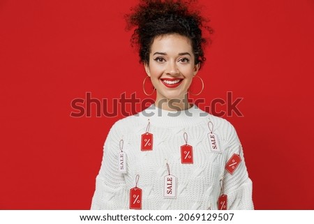 Young smiling cheerful satisfied caucasian happy female costumer woman 20s wear white knitted sweater with tags sale in store showroom looking camera isolated on plain red background studio portrait
