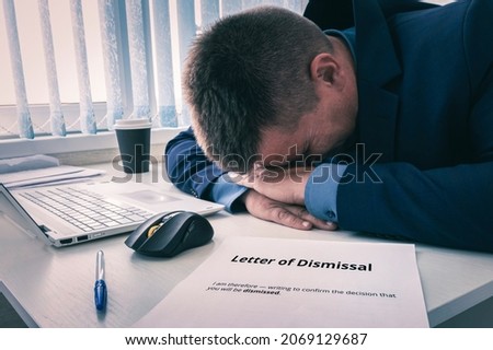 An employee opens a letter of resignation at the workplace. The boss fires employees. A letter of dismissal on a white desktop and a crying employee. Royalty-Free Stock Photo #2069129687