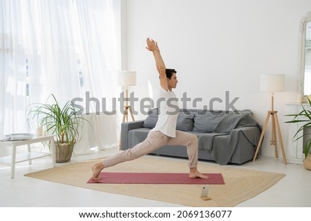 Sporty Young Man is Making Lunge Warrior Yoga Pose in Living Room at Home. Male is Stretching Him Legs. Boy is Making Physical Exercises. Home Fitness, Yoga Practice, Workout And Wellness Concept Royalty-Free Stock Photo #2069136077