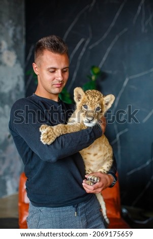 Young man holding a little lion cub in his arms